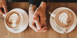 Couple holding hands on a table with coffee on each side 
